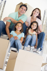 Fototapeta na wymiar Family sitting on staircase with boxes in new home smiling