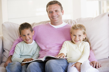 Obraz premium Man and two children sitting in living room reading book and smi