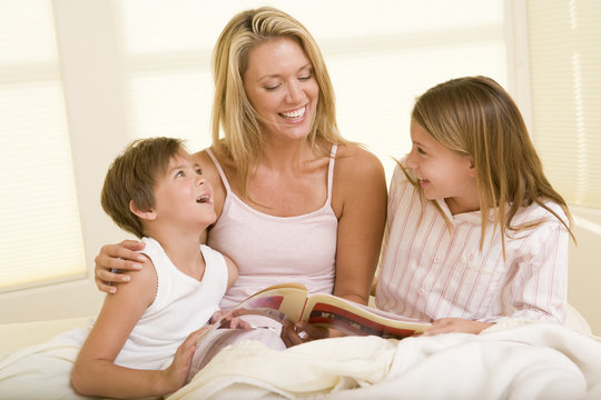 Woman with two young children sitting in bed reading book and sm