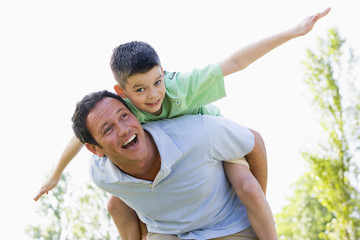 Man giving young boy piggyback ride outdoors smiling © Monkey Business