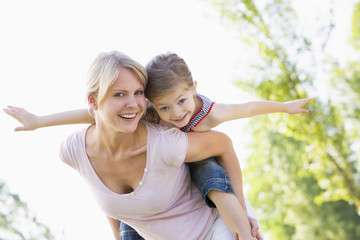 Woman giving young girl piggyback ride outdoors smiling