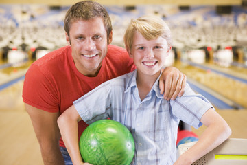 Fototapeta premium Man and young boy in bowling alley holding ball and smiling