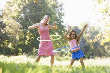 Woman and young girl outdoors using hula hoops and smiling - obrazy, fototapety, plakaty