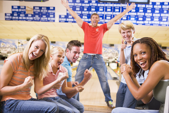 Family In Bowling Alley With Two Friends Cheering And Smiling