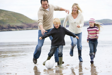 Family playing soccer at beach smiling
