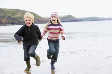 Fototapeta na wymiar Two young children running on beach holding hands smiling