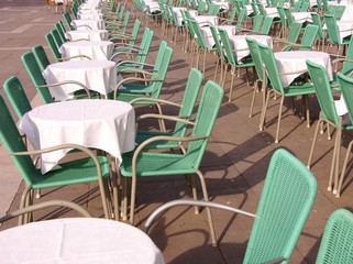 A terrace with green chairs and round tables