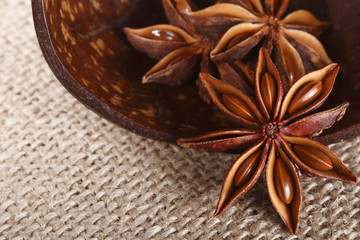 anis star in a wooden cup on burlap canvas background, close-up