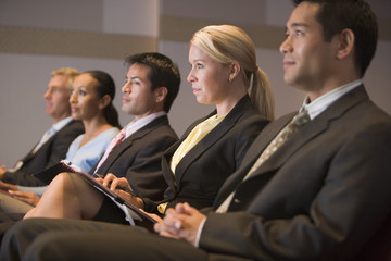 Five businesspeople sitting in presentation room with clipboards