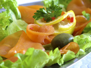 Smoked fish slices, arrangement with some vegetables on a plate