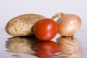 A potato, tomato, and an onion reflected on aluminum foil