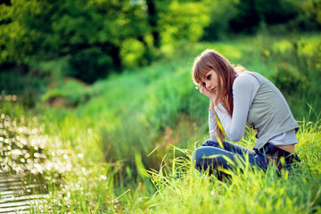 Dreaming girl sitting in green grass on lakeside