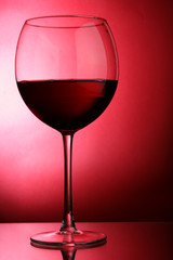 Glass of red wine close-up over red background