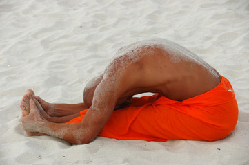 Tanned white man practicing yoga on the beach