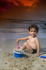 boy play with sand on the beach at sunset