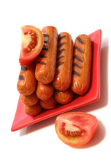 grilled sausages on red dish with two tomatoes quarter