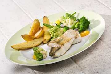 grilled Zander, fried potatoes and various vegetables on a plate