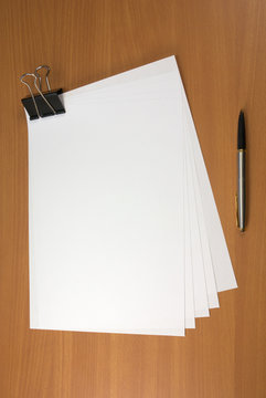 Blank papers and pen on wooden table surface.