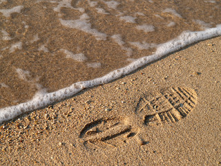 Fototapeta na wymiar Shoe-print in wet sand with wave