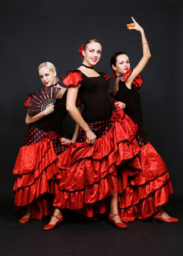 Three Dancers In Spanish Dresses Over Dark Background