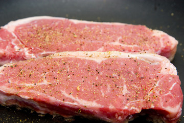Seasoned strip steaks in a pan ready for cooking