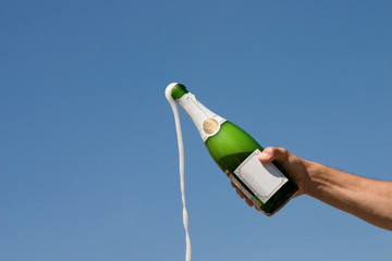Hand holding bottle of champagne on a background of the blue sky