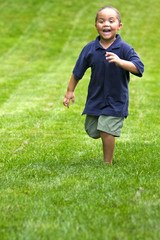 Happy mixed race boy running through green grass