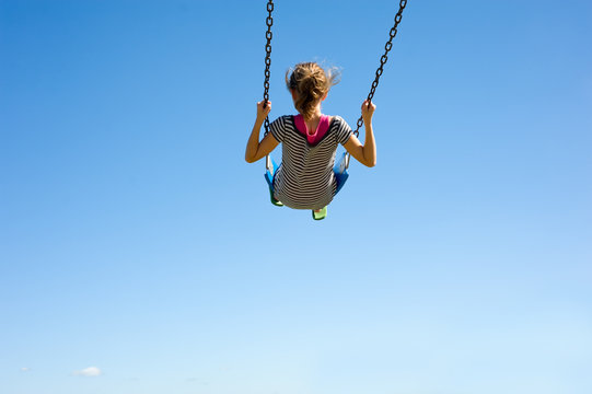 A young girl playing on a swingset in front of a blue sky