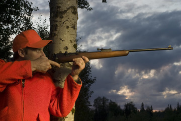 hunter leaning on tree and aiming rifle