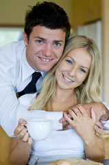 A young man hugs his wife who is sat having breakfast at home
