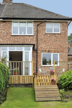 house with wooden decking and patio leading to garden