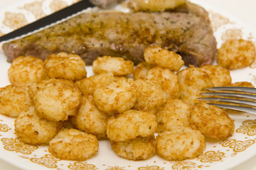 A broiled strip steak on a plate with fried potatoes