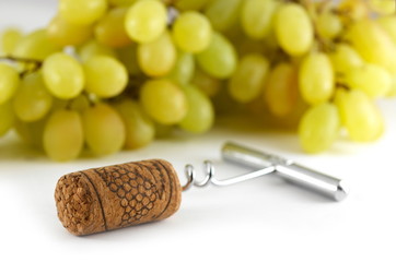 Corkscrew with wine cork and white grapes background