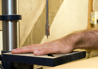 A hand under a drill press, symbolizing work safety