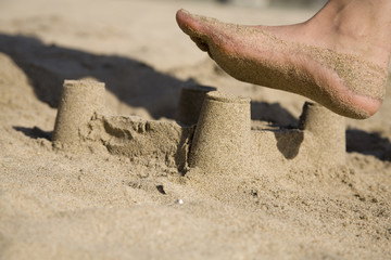 A sand castle at the beach about to be destroyed by a foot