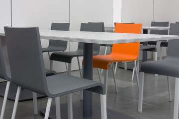 Orangefarbener Stuhl unter grauen Stühlen und Tischen
