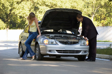 The guy repairs the car, the girl looks at him and smiles