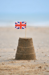 A sandcastle with a union jack flag on beach.