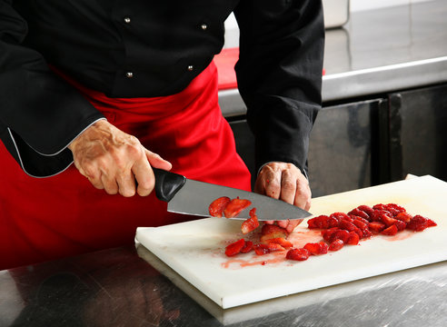 Chief in black cuts strawberry on professional kitchen