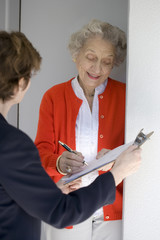 Attractive senior woman signing a document at her front door