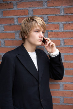 Teenage boy using mobile phone by brick wall