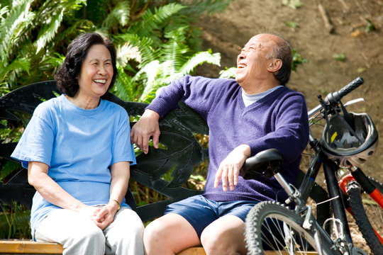 A Shot Of Senior Asian Couple Sitting On A Bench At A Park