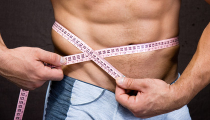 Young pretty man measuring his perfect body isolated on braun