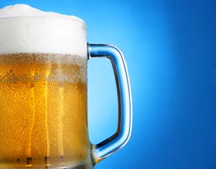 Poster Mug of beer close-up with froth over blue background © Roman Sigaev