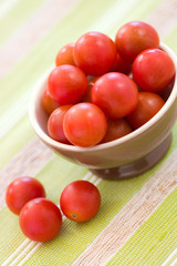 Cherry tomatoes in a brown bowl on a green background