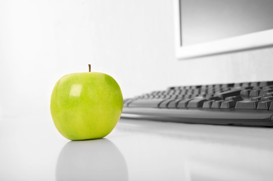 Green apple is on a table on a background of a pc
