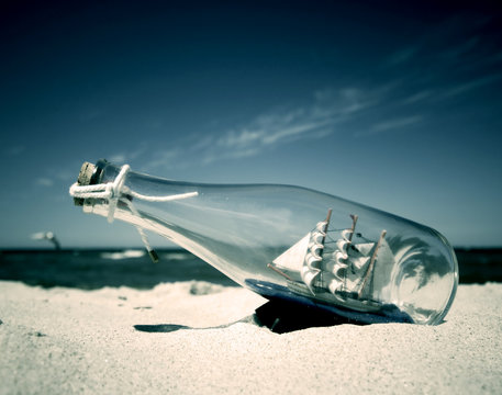 Bottle with ship inside lying on the beach. Conceptual image