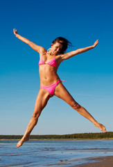 Woman in pink bikini jumps high on a beach