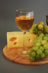 Glass of wine, cheese and grapes on a wooden board