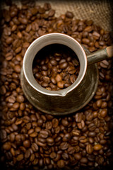 Cezve with freshly roasted coffee beans on sackcloth